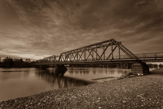 Old railway bridge across the river. Cloudy sky.