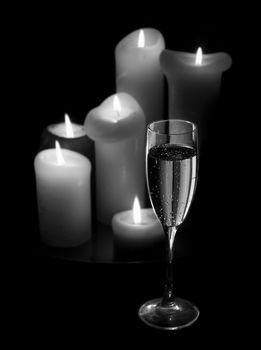 A glass of champagne in front of candles. The picture is black and white.