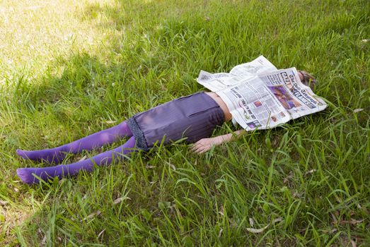 young woman lying on the grass with a newspaper in her face