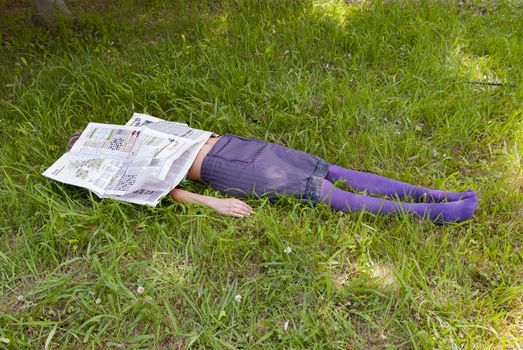 young woman lying on the grass with a newspaper in her face