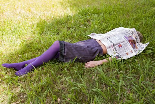 young woman lying on the grass with a newspaper in her face