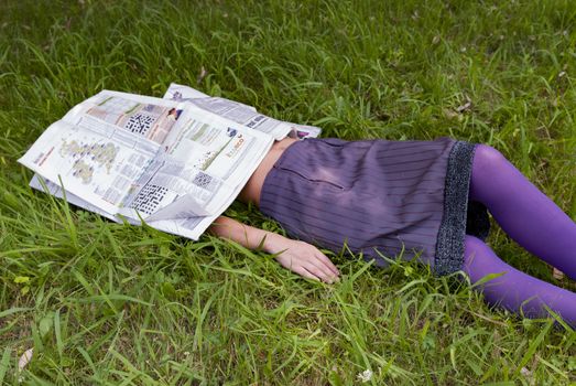 young woman lying on the grass with a newspaper in her face