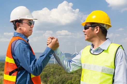 Architect and Engineer shake hand beside wind Turbine Power Generator Field as Project Development Company Agreement Joint Venture concept.