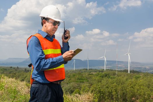Male Architect or Engineer, use Hand-Held Transceiver Radio and Digital Wireless Tablet Device, working at Wind Turbine Power Generator Field as Infrastructure Construction Project Development
