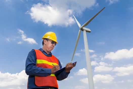 Electric Engineer writing Maintenance report on Clipboard with Wind turbine power Generator Tower Background as Green energy or Renewable Energy Technology Project Development Concept.