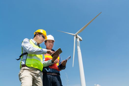 Alternative Power or Renewable Energy Technology Project Development Concept, Engineer and Architect discuss over Digital Wireless Tablet and Clipboard while working at Wind Turbine Power Generator Tower site.