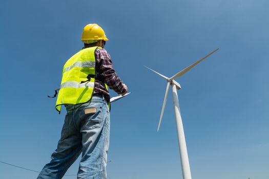 Electric Engineer writing Maintenance report on Clipboard with Wind turbine power Generator Tower Background as Green energy or Renewable Energy Technology Project Development Concept.