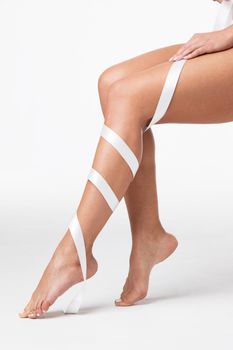 Closeup of perfect women's legs with white ribbon on white background