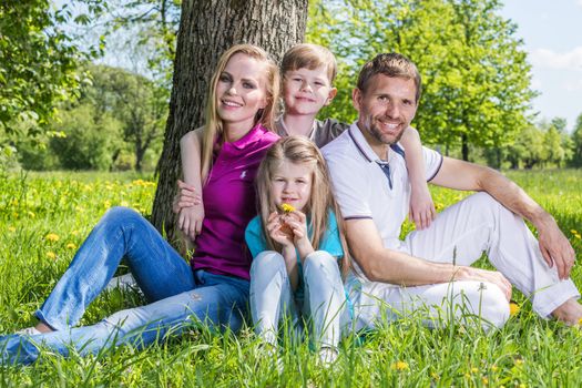 Happy family with man, woman and two children leaning on tree in city park