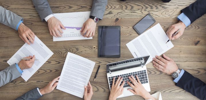 Business team working with contract, financial reports and laptop dicussing deal sitting around office table