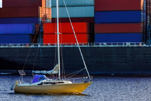 Yellow sailboat traveling against the cargo ship in Riga