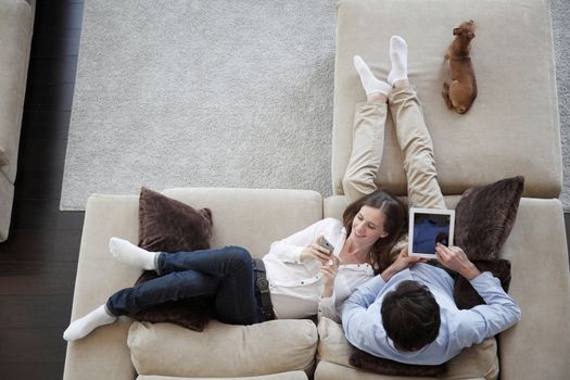 Couple using digital tablet at home sitting on sofa, top view