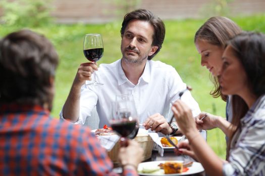Friends clink glasses of red wine at outdoor dinner