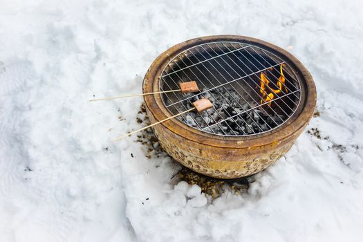 Barbeque snacks using a fire bowl in cold winter snow.