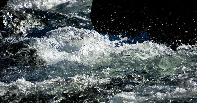 Raging river rapids splashing against a rock with white foamy froth