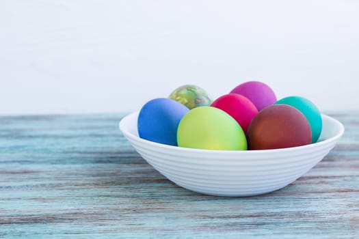 White plate of Easter multicolored boiled eggs decoration on wooden background