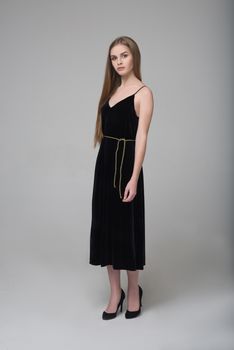 Young beautiful long-haired female model poses in long black dress on grey background