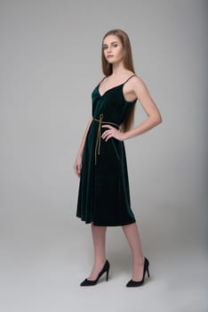 Young beautiful long-haired female model poses in dark green dress on grey background