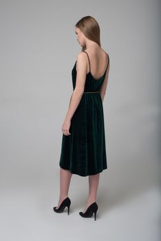 Young beautiful long-haired female model poses in long black dress on grey background