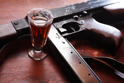 Old USA submachine gun closeup near glass of whiskey on wooden background