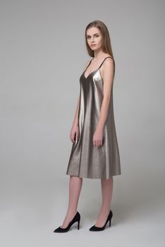 Young beautiful long-haired female model poses in silver grey dress on grey background