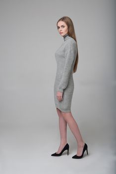 Young beautiful long-haired female model poses in grey knitted dress