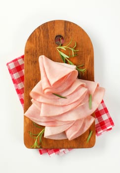 thin slices of ham and fresh rosemary leaves on wooden cutting board