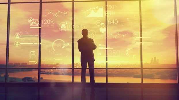 Silhouette of a man in a huge office in front of large windows viewing corporate infographics.