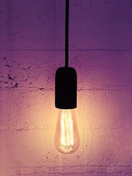 Industrial design light bulb on a black cord. Warm purple light.