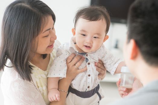 Daddy showing milk bottle to baby boy. Happy Asian family at home, candid living lifestyle indoors.