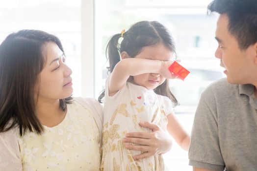 Parents comforting crying daughter. Asian family at home, natural living lifestyle indoors.