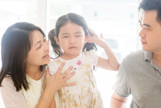 Parents comforting crying child. Asian family at home, natural living lifestyle indoors.