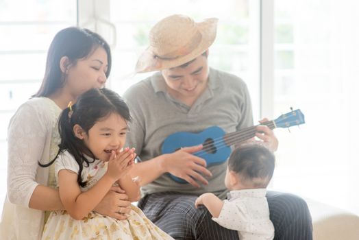 Parents and children singing and playing ukulele together. Asian family spending quality time at home, natural living lifestyle indoors.