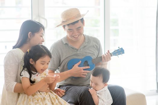 Parents and children singing and playing music instruments together. Asian family spending quality time at home, natural living lifestyle indoors.