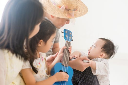 Parents and children playing music instruments together. Asian family spending quality time at home, natural living lifestyle indoors.