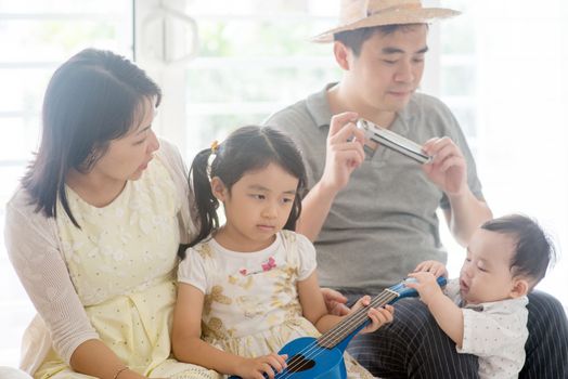 Parents and children singing and playing ukulele and harmonica together. Asian family spending quality time at home, living lifestyle indoors.