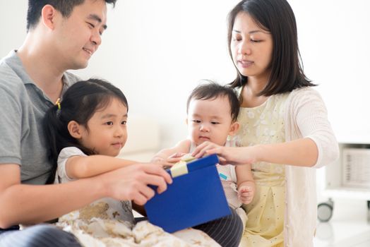 Parents and children open gift box together. Asian family spending quality time at home, natural living lifestyle indoors.