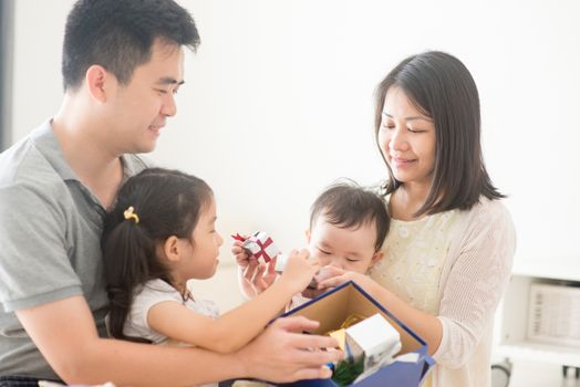 Parents and children open Christmas gift together. Asian family spending quality time at home, natural living lifestyle indoors.