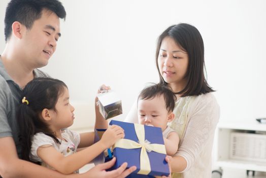 Parents and children open present box together. Asian family spending quality time at home, natural living lifestyle indoors.