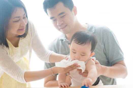 Mother blow baby nose with tissue paper. Asian family spending quality time at home, living lifestyle indoors.