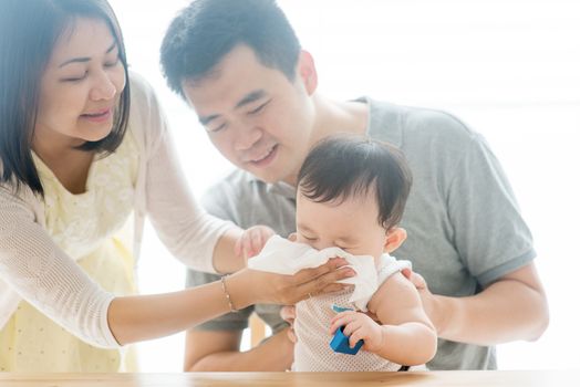 Mother wipes baby nose with tissue paper. Asian family spending quality time at home, living lifestyle indoors.