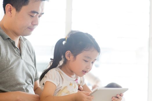 Father using touchscreen tablet PC with child on sofa. Asian family at home, living lifestyle indoors.
