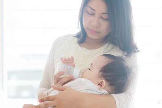 Mother bottle feed formula milk to 9 months old child. Asian family at home, living lifestyle indoors.