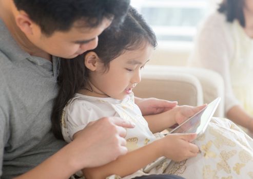 Father and daughter using digital tablet on sofa. Asian family at home, living lifestyle indoors.