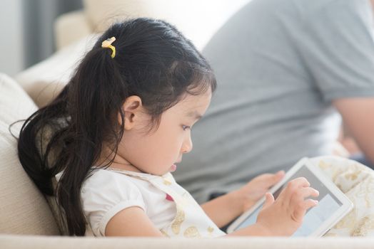 Little girl using digital tablet on sofa. Asian family at home, living lifestyle indoors.