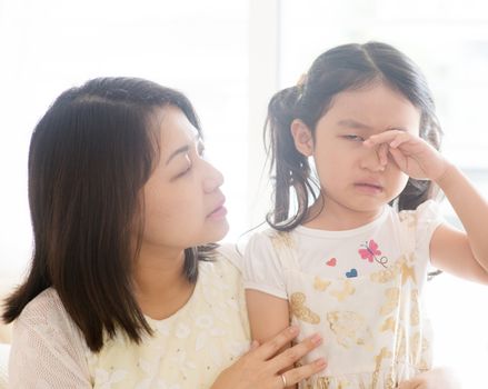 Mother comforting crying daughter. Asian family at home, living lifestyle indoors.
