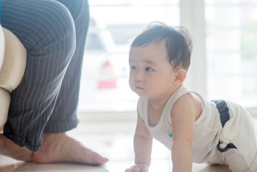 Nine months old baby boy crawling towards father. Asian family at home, living lifestyle indoors.