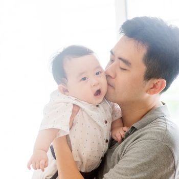 Happy Asian family at home. Father kissing baby boy, living lifestyle indoors. 