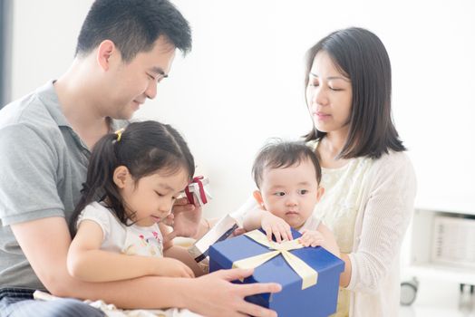 Parents and children opening gift box together. Asian family spending quality time at home, living lifestyle indoors.