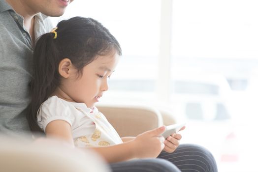Father and child using digital tablet on sofa. Asian family at home, living lifestyle indoors.
